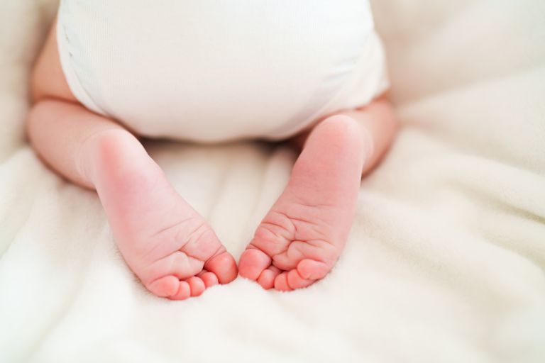 Image of the back of a baby and a baby's feet laying on a rug. 