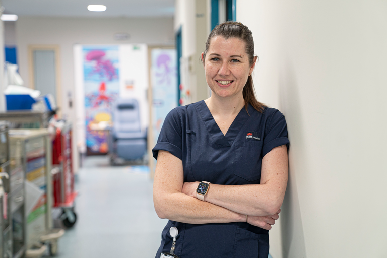 Nurse leaning against a wall with arms crossed smiling