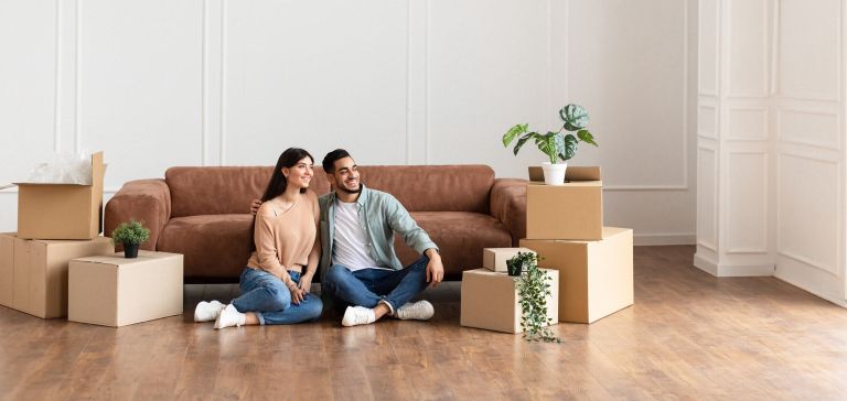 Couple sitting on floor with moving boxes and furniture.