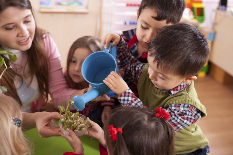 Preschool aged children watering a plant with their educator 