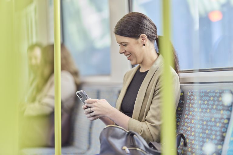 A person holding a smartphone while sitting in a train carriage.