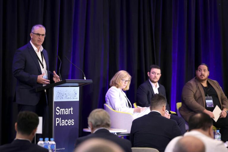 A facilitator and panel on stage in front of an audience at a SmartNSW Masterclass event.