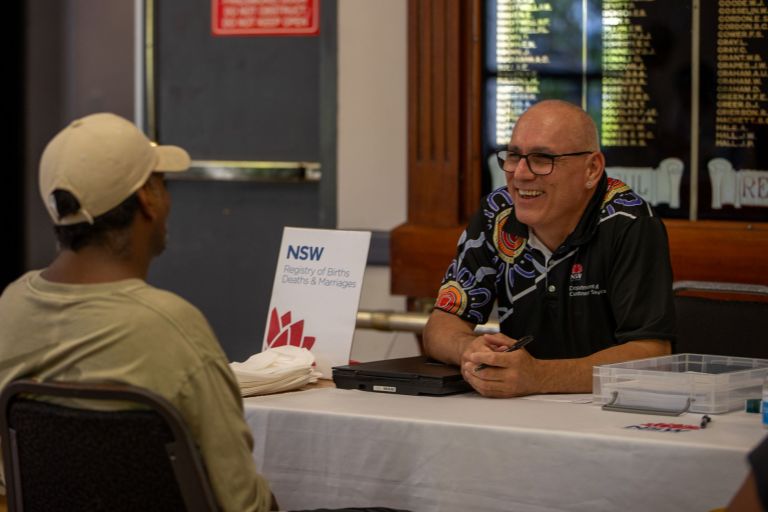 A service representative sits at a desk, smiling across at a man visiting the event
