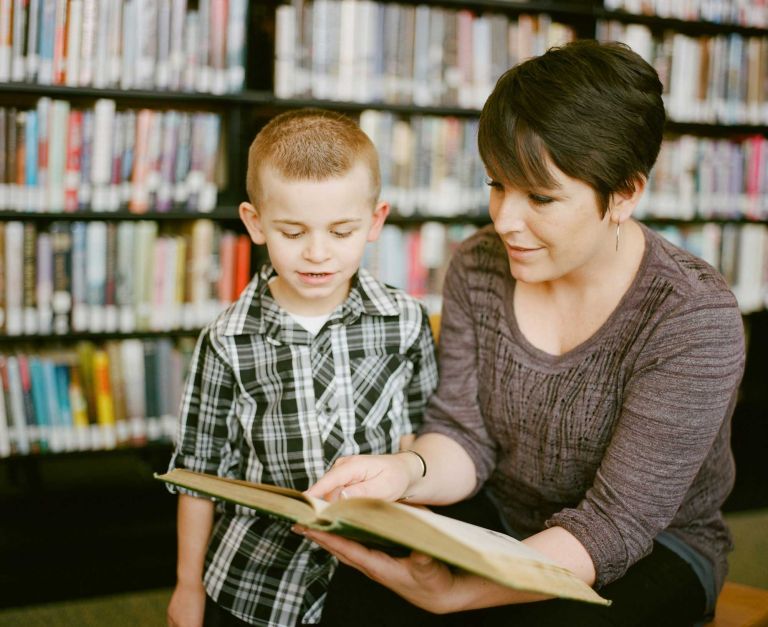 A woman reads a book to a boy in a school library