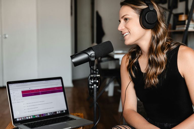 A woman speaks into a microphone, recording a podcast