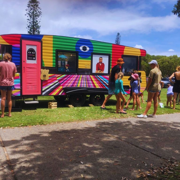 The museum on wheels, a rainbow coloured caravan with people around it