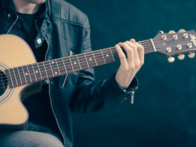 Person wearing a leather jacket playing an acoustic guitar