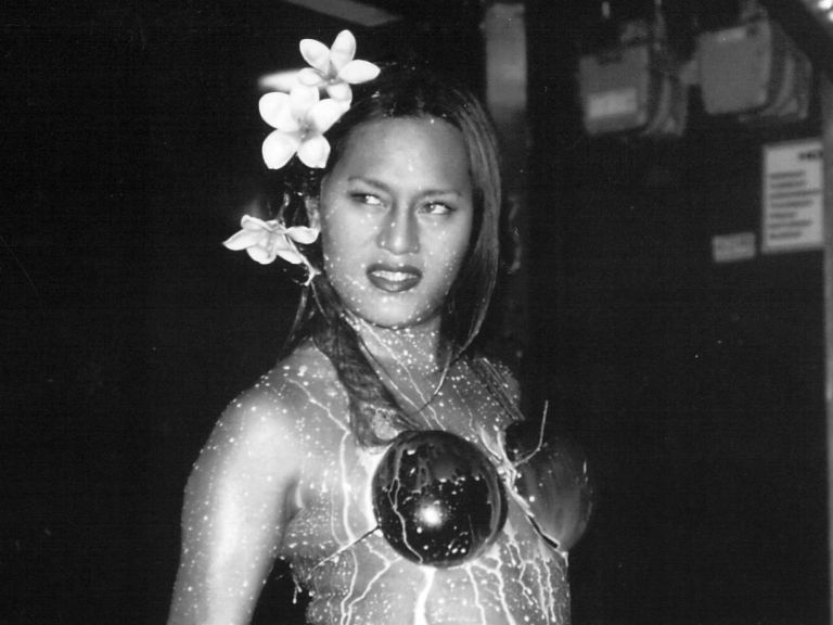 A black and white image of a person with coconut shells on their chest and flowers in their hair.