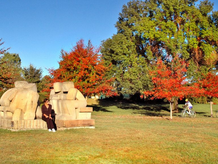 2 sandstone sculptures of people sitting down talking in the park.