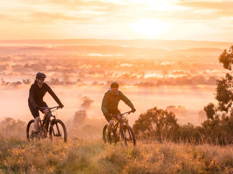 Two cyclist at the peak of a reserve during a glowing sunrise