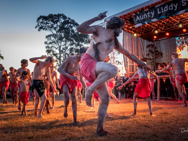 Male Aboriginal dancers dance in front of a stage.