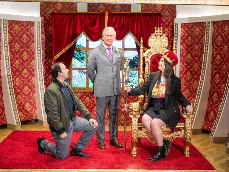 One guest kneels while the other sits on a throne next to the King's wax figure.