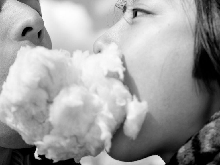 Black and white image of two people holding fairy floss between their mouths.
