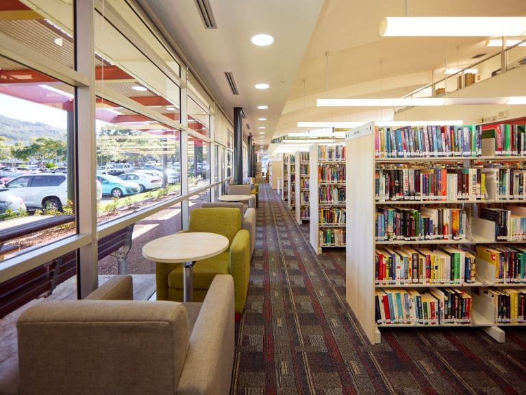 Comfortable lounge chairs and small tables adjacent to large windows and book shelves.