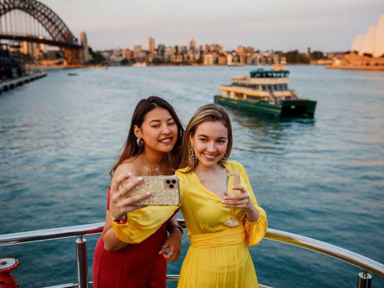 Girls taking a photo in front of Sydney Opera House onboard holding drinks