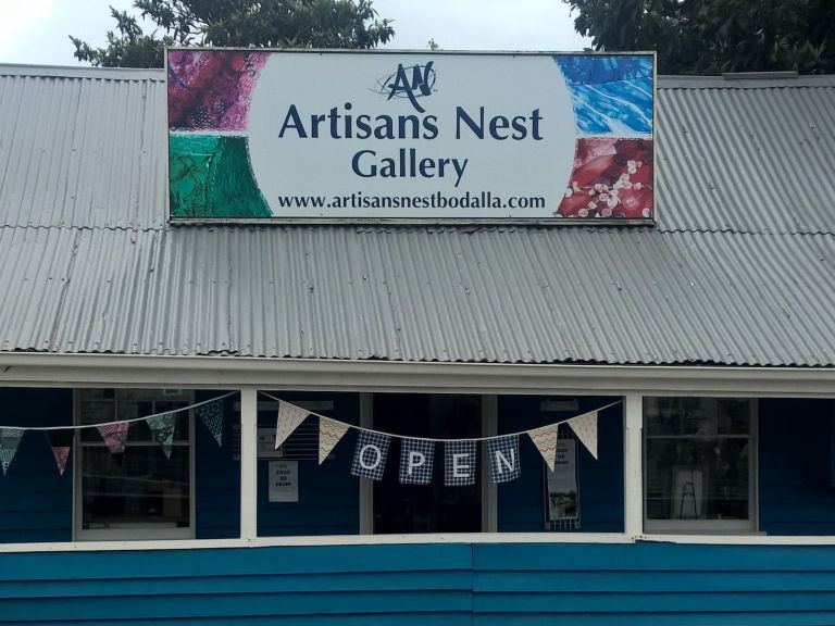 Artisans Nest Gallery exterior from highway, marine blue fence,showing roof sign and "open" Bunting