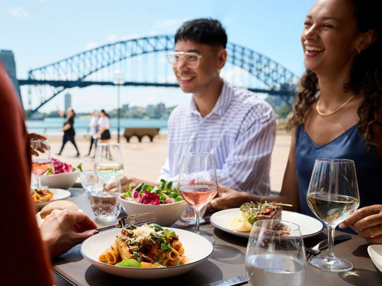a couple enjoy lunch at Portside, with Sydney Harbour Bridge and the Harbour in the background