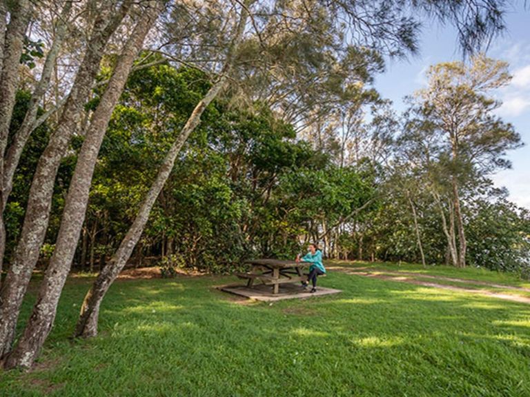 A woman sitting at a picnic table surrounded by trees in Brunswick River picnic area, Brunswick