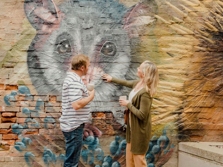 A man and woman touch a mural of a possum on a brick wall in Memorial Plaza, Corowa.