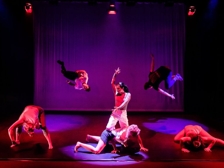 A production image from a performance of Collision. People flip in the background