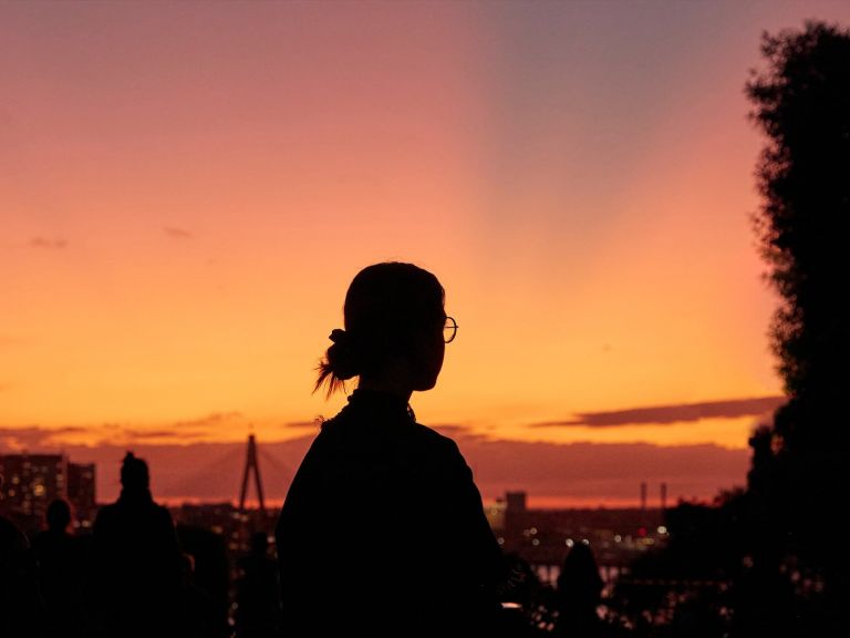 Silhouette of a person wearing glasses staring into the distance with a sunset in the background