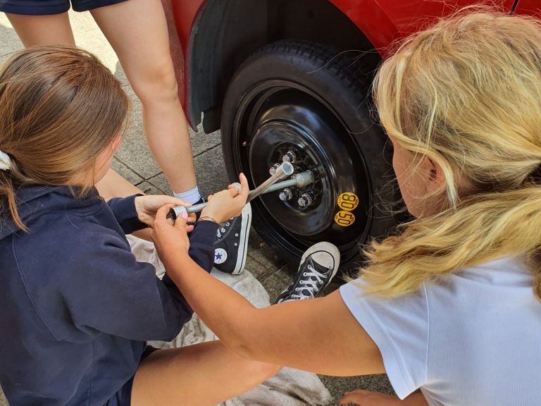 girls changing the tyre on a red car