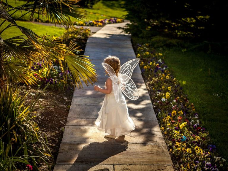 Small child walks along path with a white dress and fairy wings