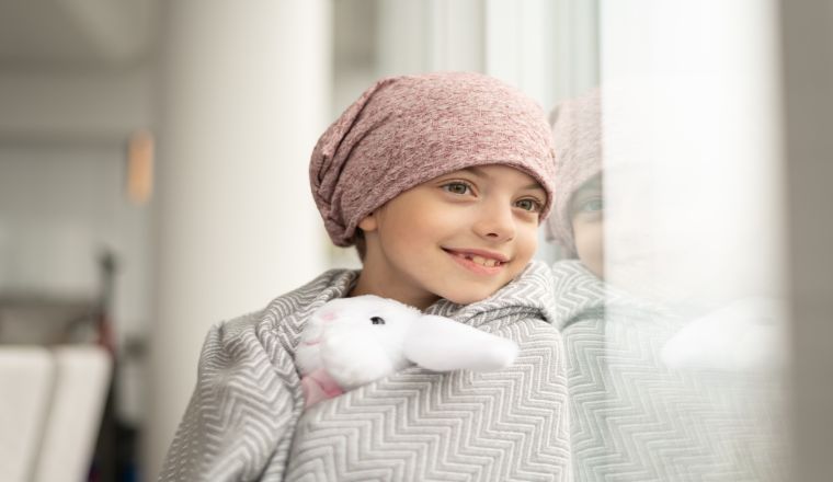 Smiling girl with cancer looks out window