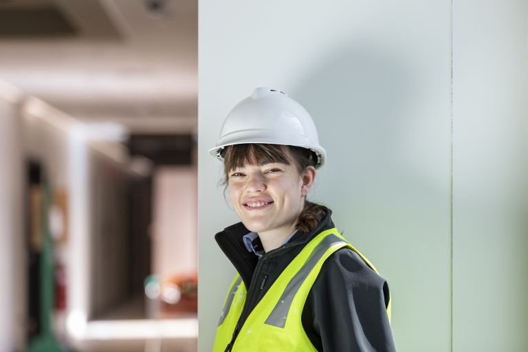 An image of Alice wearing hi vis and a hard hat on a construction site.
