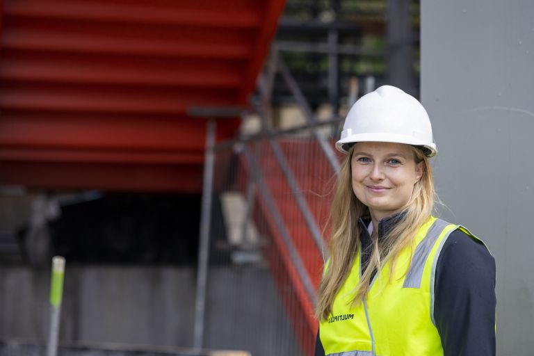 Christina is standing on a construction site smiling at the camera