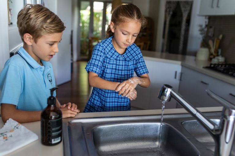 Brother and sister in school uniform washing their hands 