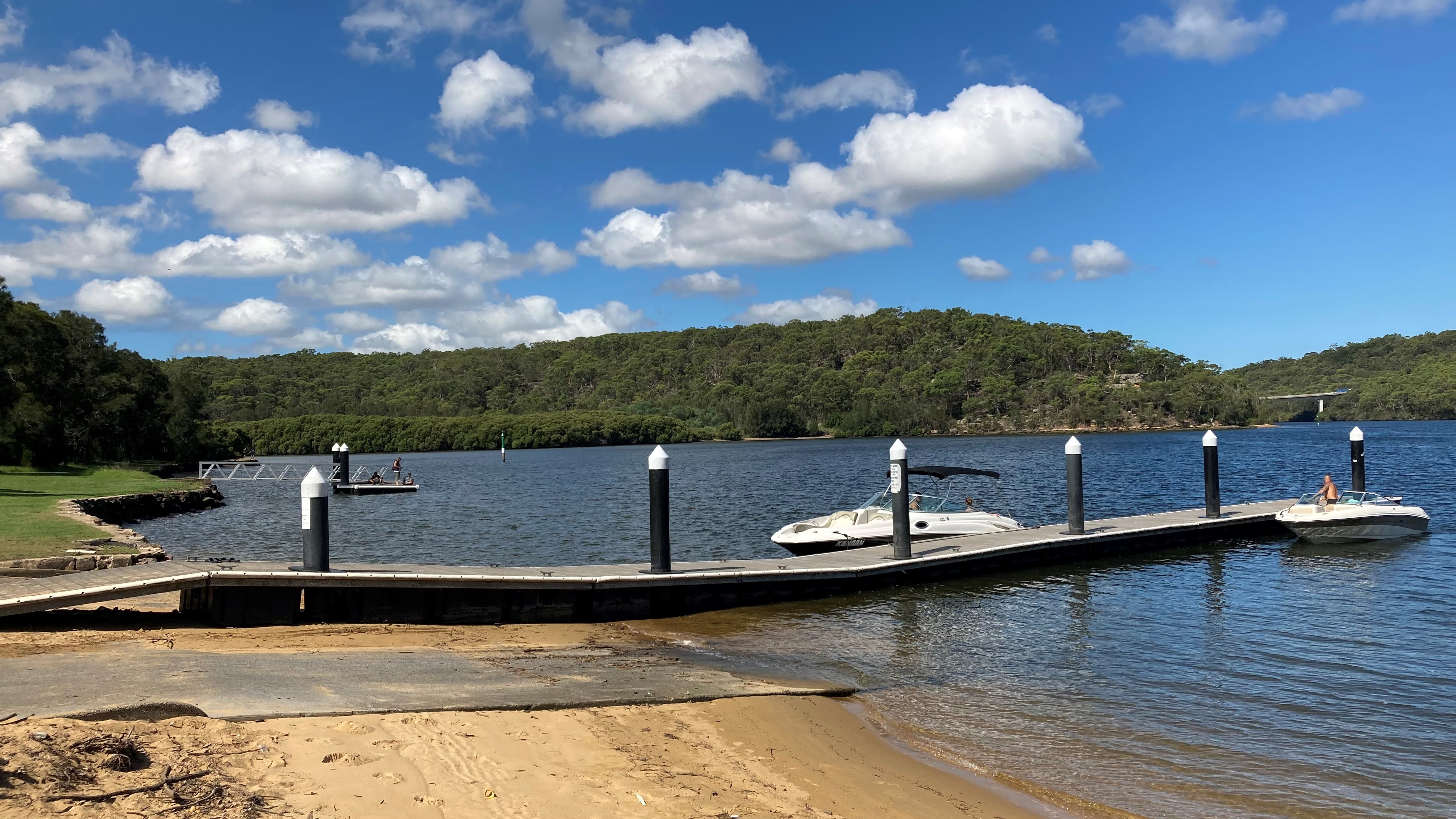 Boat ramp and jetty on a river with bushland and blue sky.