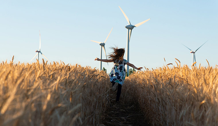 EnergyCo girl running in field of corn and windmill. 
