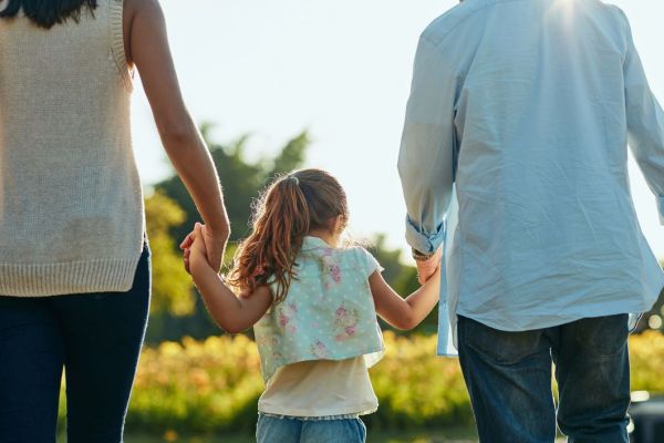 two parents and a child are holding hands, their backs are to the camera