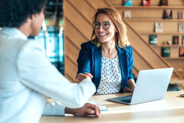 two people shake hands while sitting at an office desk