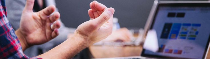 Hands open in explanation gesture in a meeting with a laptop on a table