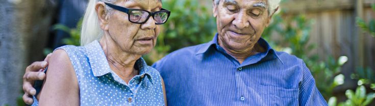 Male and female elderly Aboriginal couple reading iPad in back yard