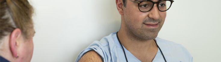 Man in blue hospital scrubs getting needle in arm