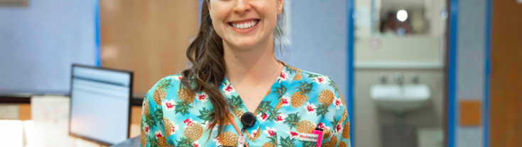 Smiling woman wearing bright shirt with pineapple pattern on, stands in hospital 