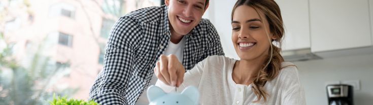 Young couple smiling and putting coins into blue piggybank