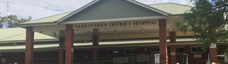 Main entrance to the Narrandera Health Service. The entrance has a ramp access to the left and steps on the right - both lead to the main entrance. A colour coded zone map of the hospital is displayed outside the main entrance. Public parking spots are shown outside as well. 