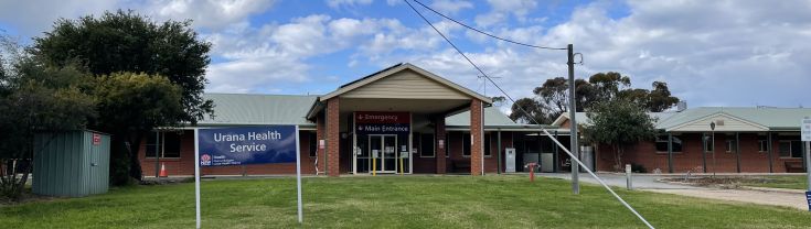 Main entrance to the Urana Multipurpose Service. A driveway is shown to the right of the image, which leads to the main and emergency entry points. A small blue sign with NSW Health logo and 'Urana Health Service' is shown to the left of the image. 