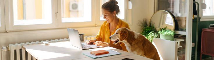 A young woman working from her home office with her pet dog.