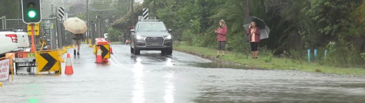 A car waits at a flooded road with emergency signage nearby.