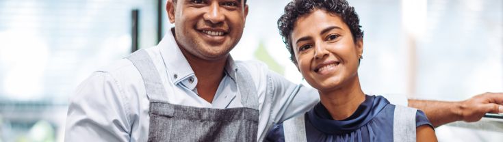 A male and female working at a cafe wearing aprons