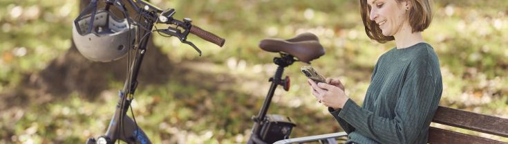 Woman sitting on a bench in a park next to an e-bike.