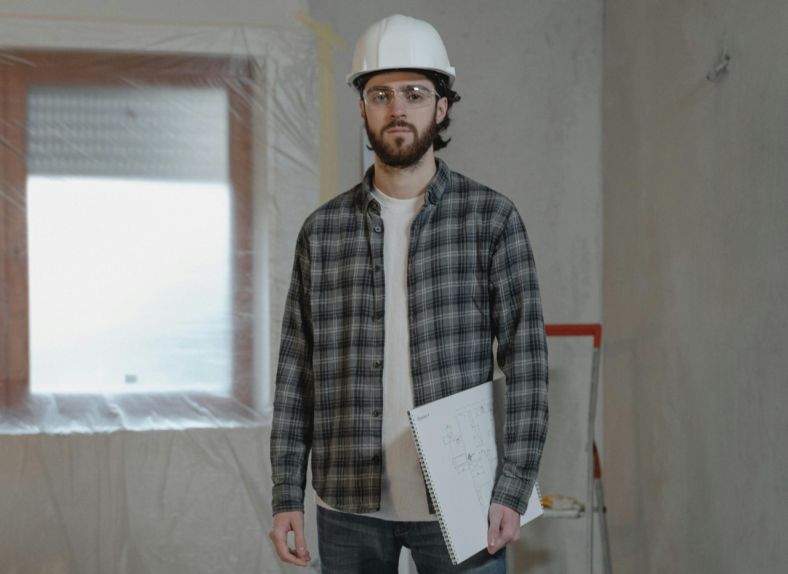 You man standing at an indoor construction site wearing a hardhat.