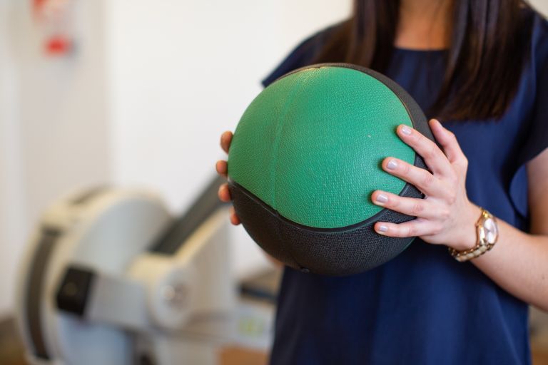 A female rehabilitation staff holds a green and black exercise ball