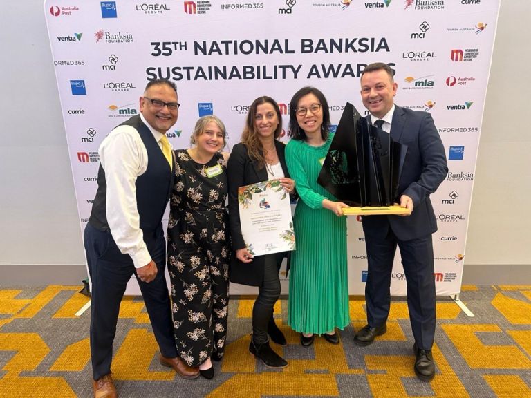 Five people stand togethr in front of a banner that reads Banksia National Sustainability Award. The man on the right holds a large black trophy, the woman in the middle holds a certificate.